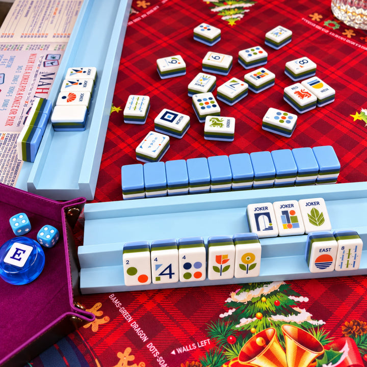 Real holiday game night setup for the Geometric American Mahjong tile set from the Artistry Collection by The Mahjong Tile, featuring light blue racks on a festive table mat.